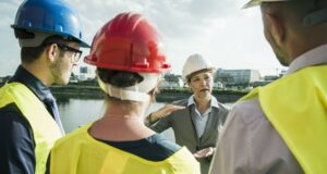 Businesswoman talking to people with safety helmets at riverside